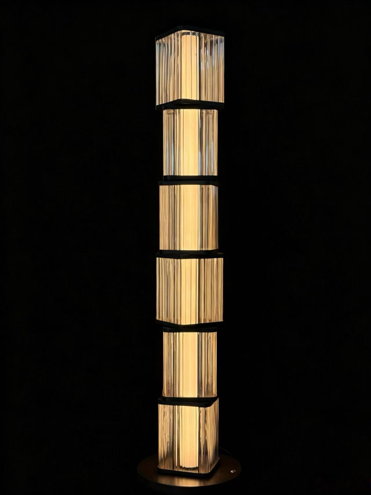 Column floor light with stacked transparent ribbed sections and dark divider rings on a round base in the workshop