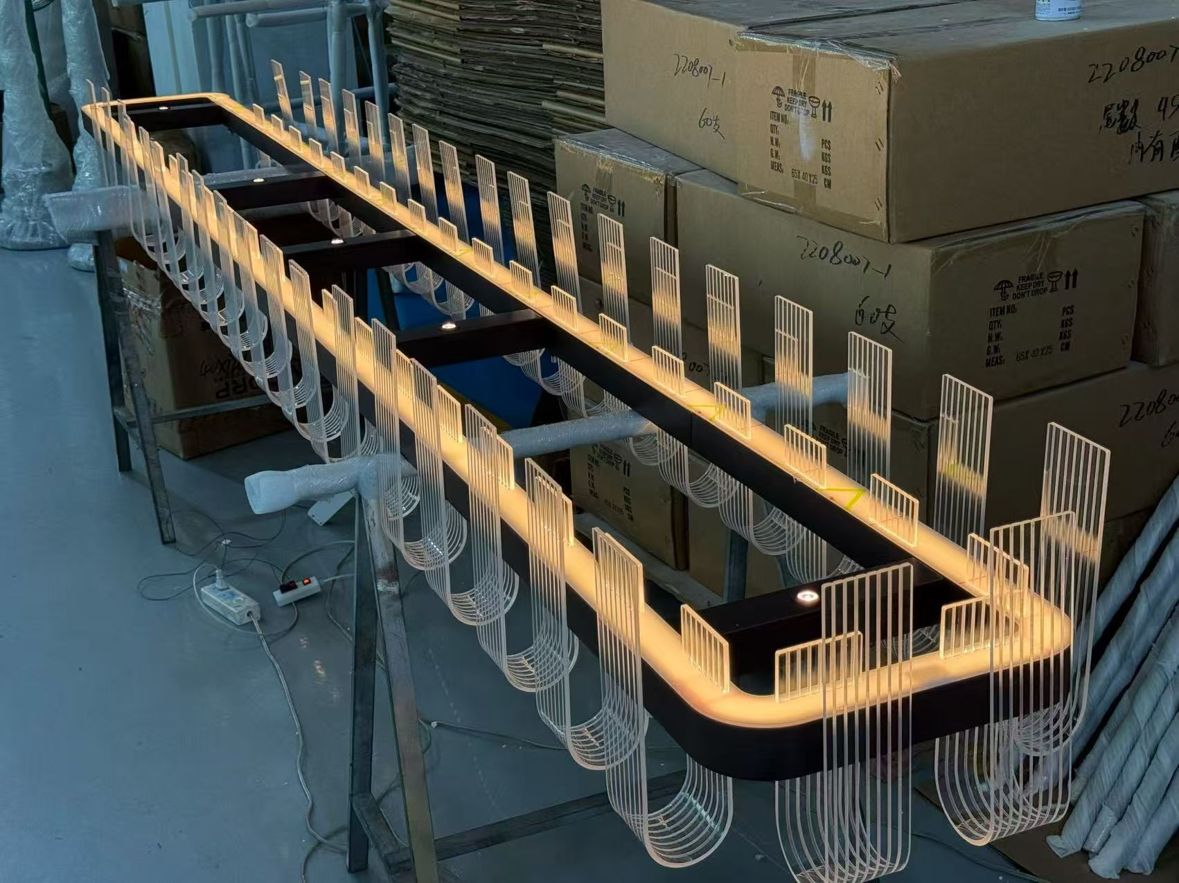 Elongated dark open-frame chandelier with transparent vertical and U-shaped elements in the workshop