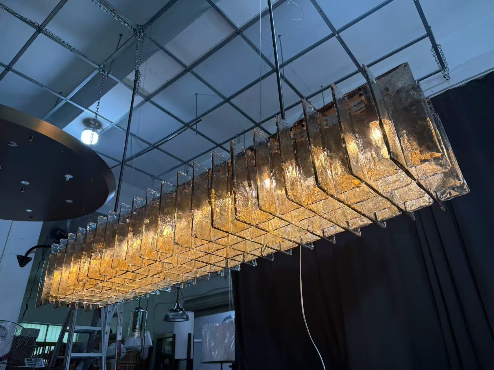 Long chandelier formed from repeated smoked textured glass elements during a workshop test