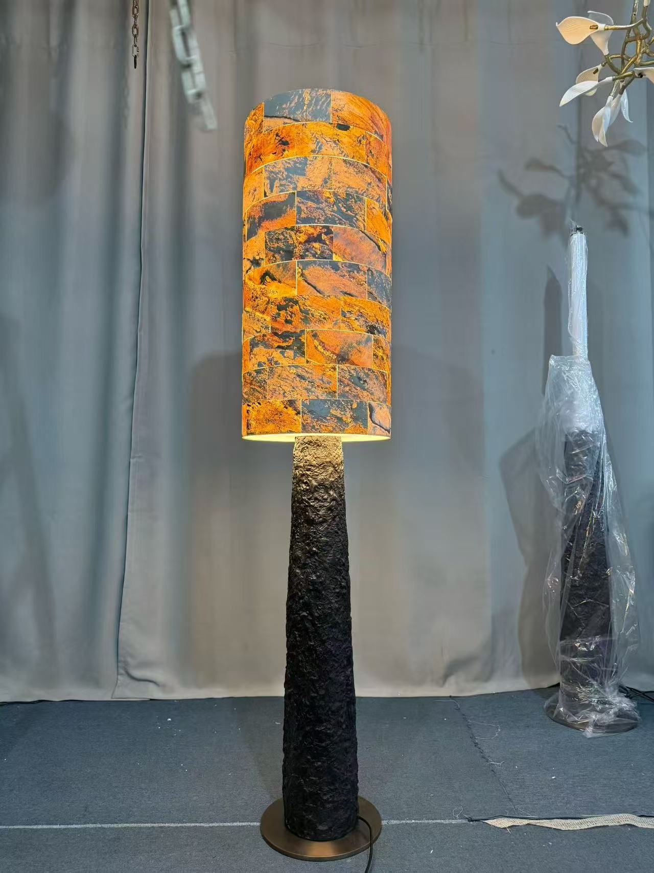 Tall floor light with an orange patterned cylindrical shade, textured dark stem and round metal base in the workshop