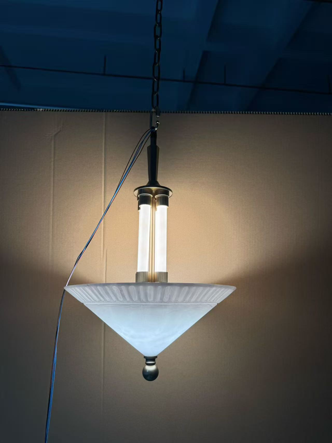 Illuminated bowl-shaped suspended light beneath a defined dark vertical structure in the workshop