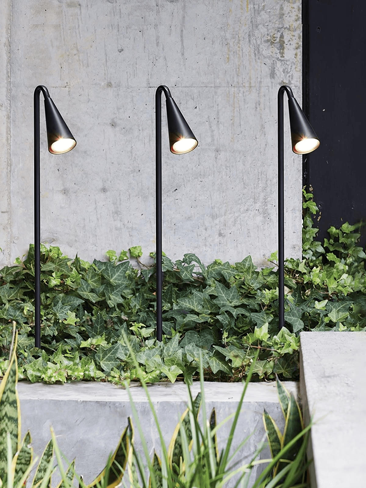 Three custom curved black garden stake lights illuminating hotel landscape planting.