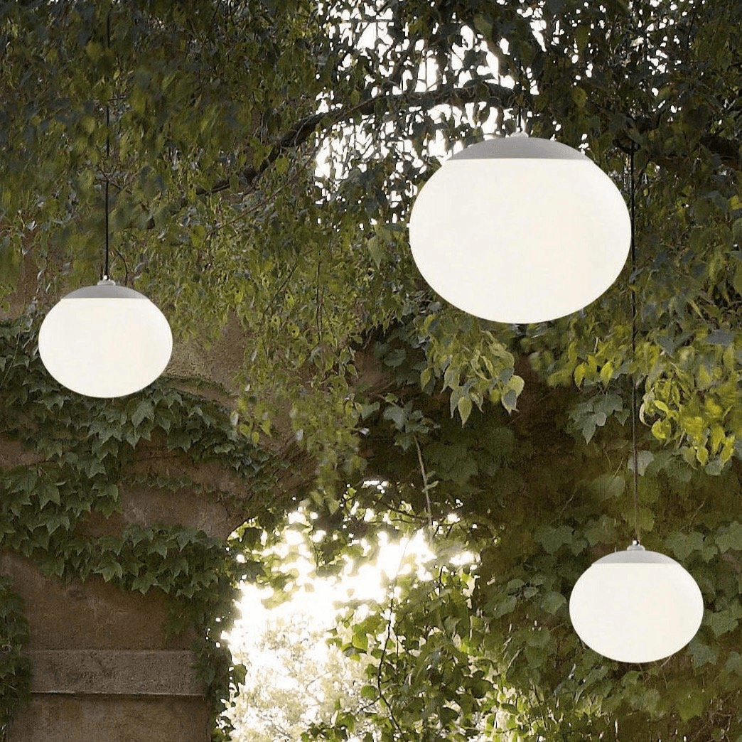 Three custom opal globe landscape lights suspended among mature trees in a garden.