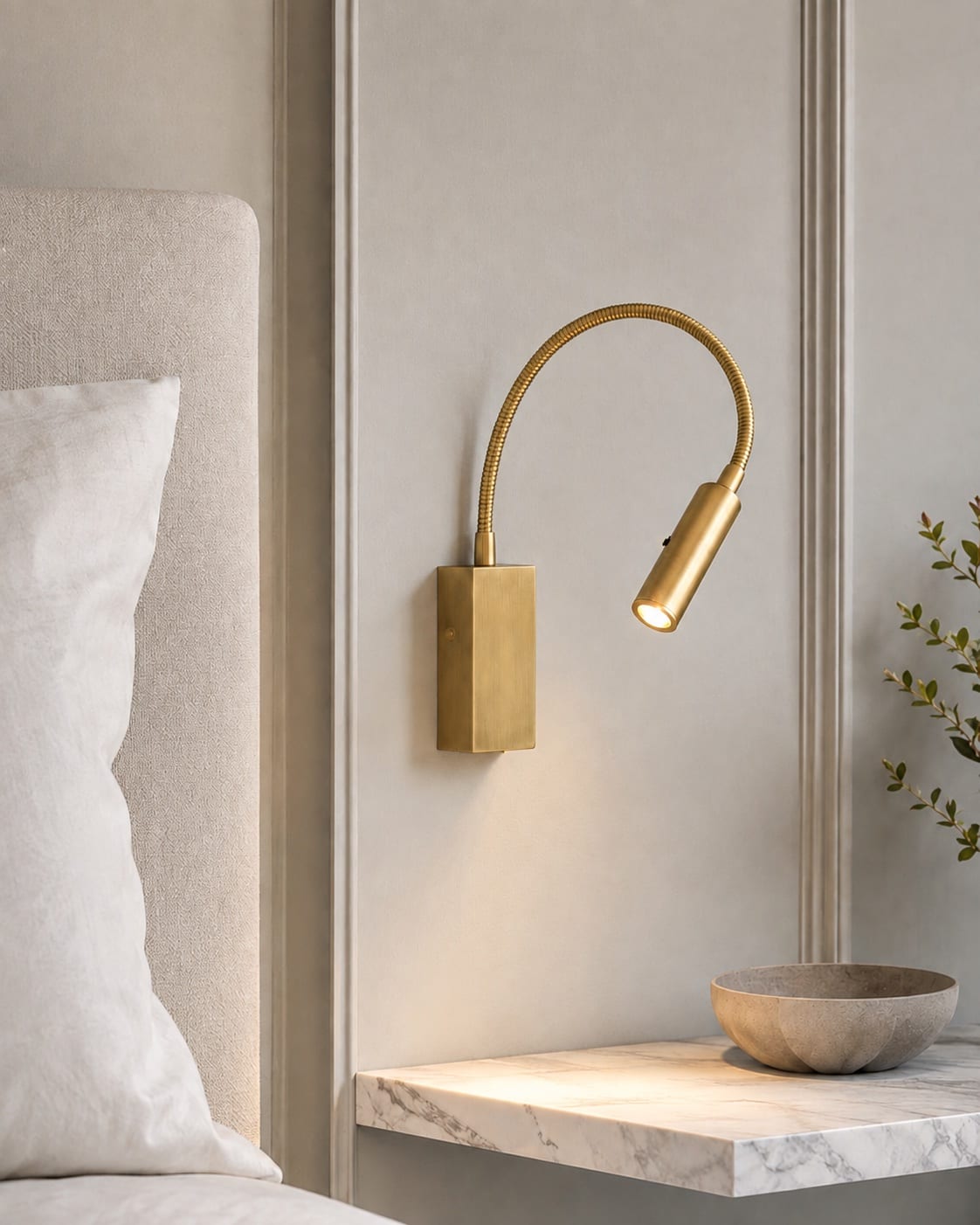 Flexible brushed brass bedside reading light mounted beside a light upholstered headboard