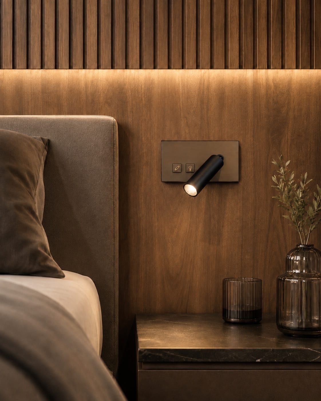 Compact black reading spotlight integrated into a bronze headboard control plate beside a hotel bed